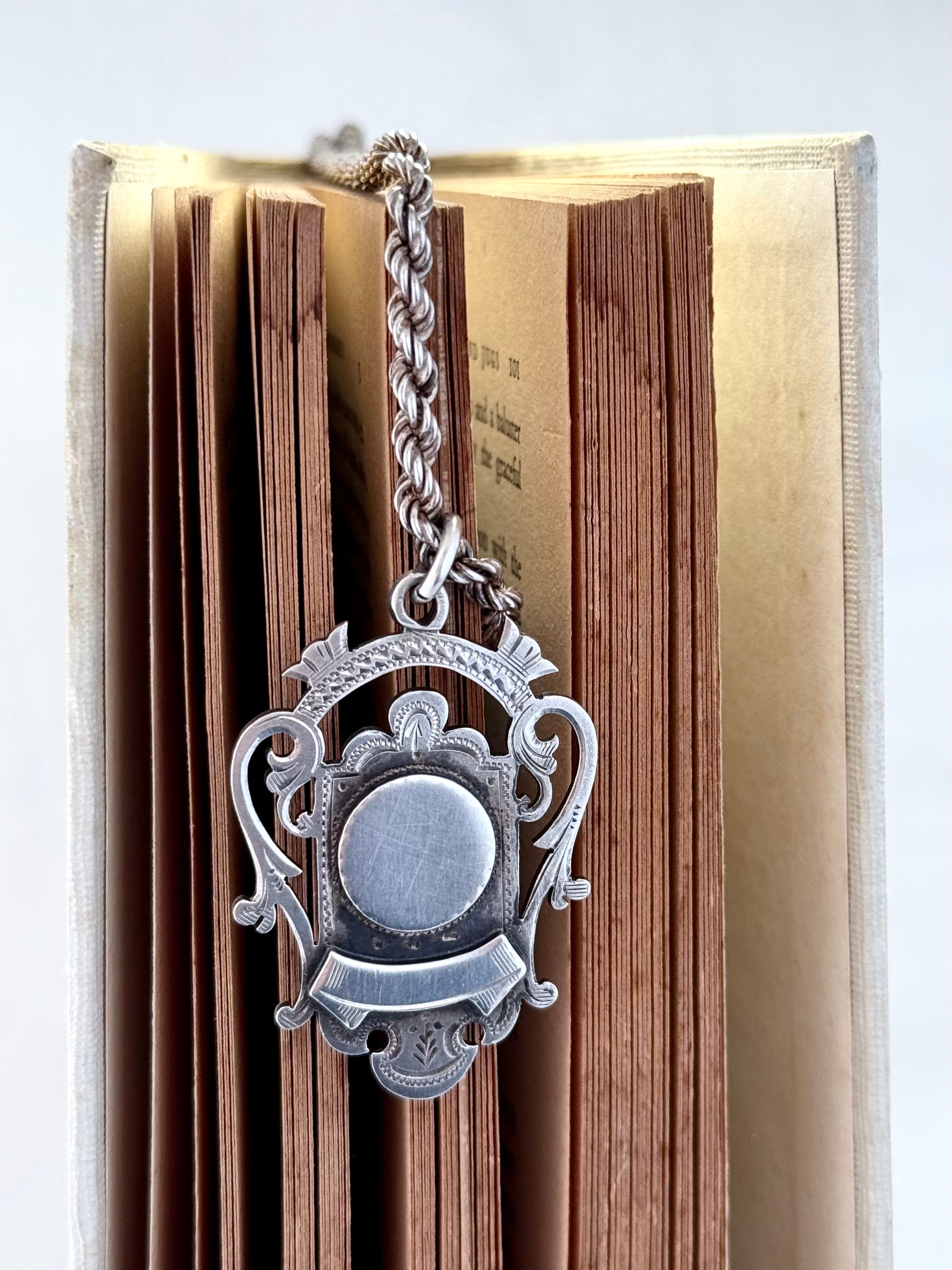 antique Silver fob medallion on thick silver chain necklace hanging on a book background