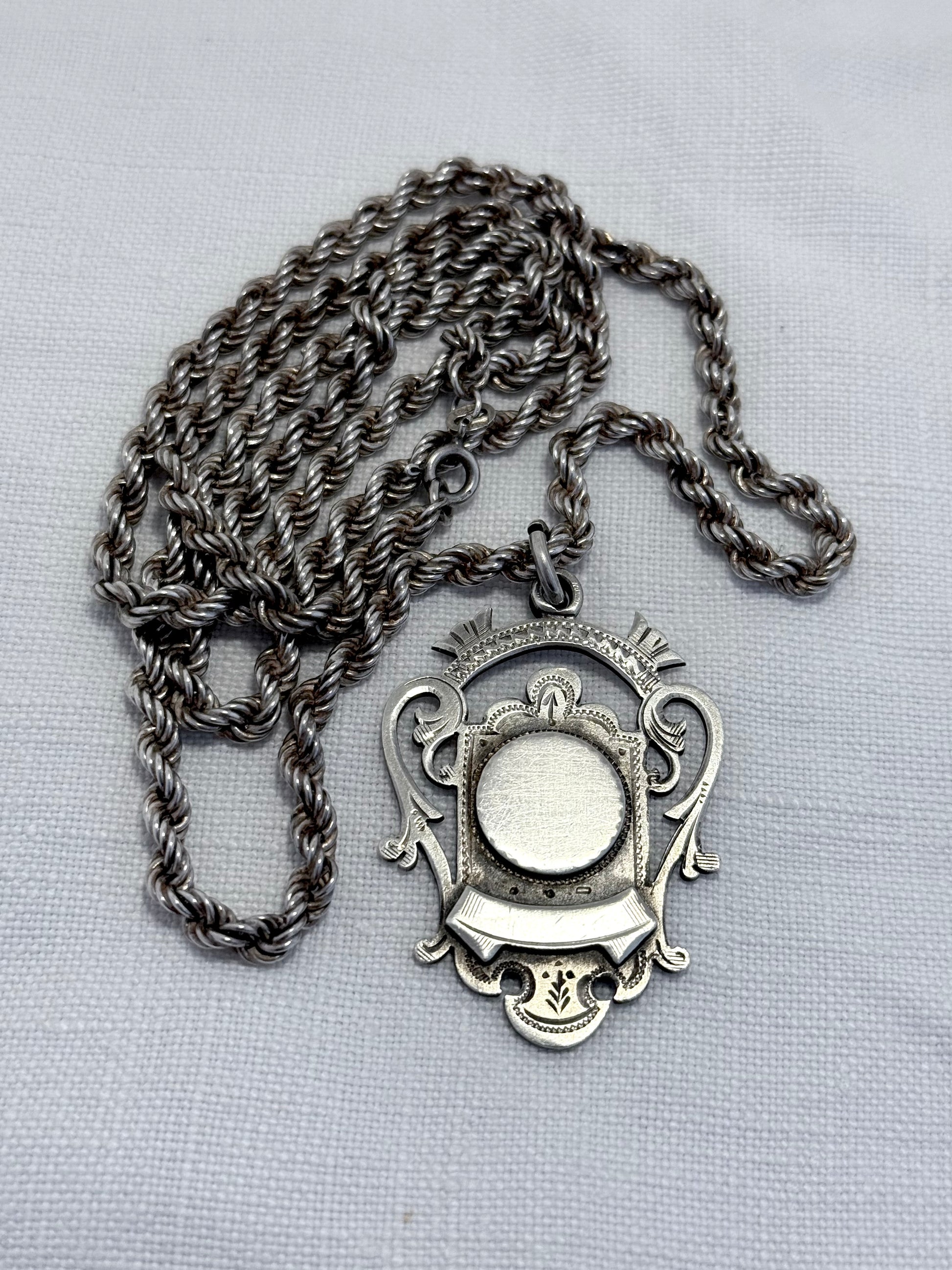 antique Silver fob medallion on thick silver chain necklace on a light gray background